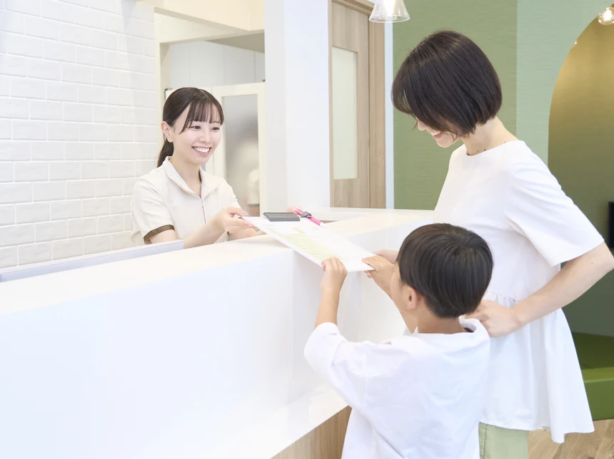 受付でスタッフに問診票を手渡す親子